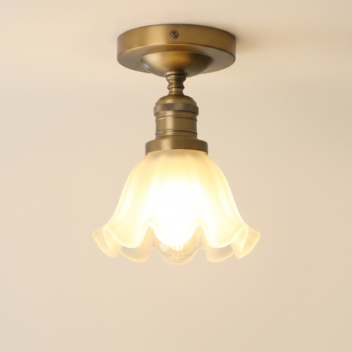 Hoxne semi flush ceiling light in antique brass with a frosted ruffled tulip glass shade, lit, cream background