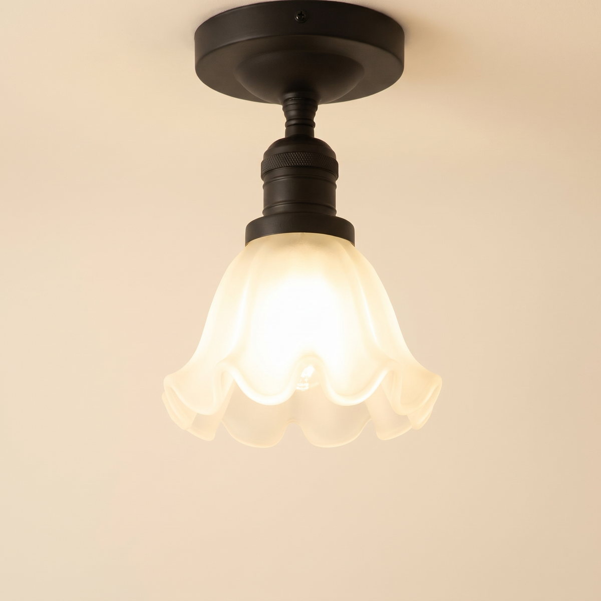 Hoxne semi flush ceiling light in black with a frosted ruffled tulip glass shade, lit, cream background