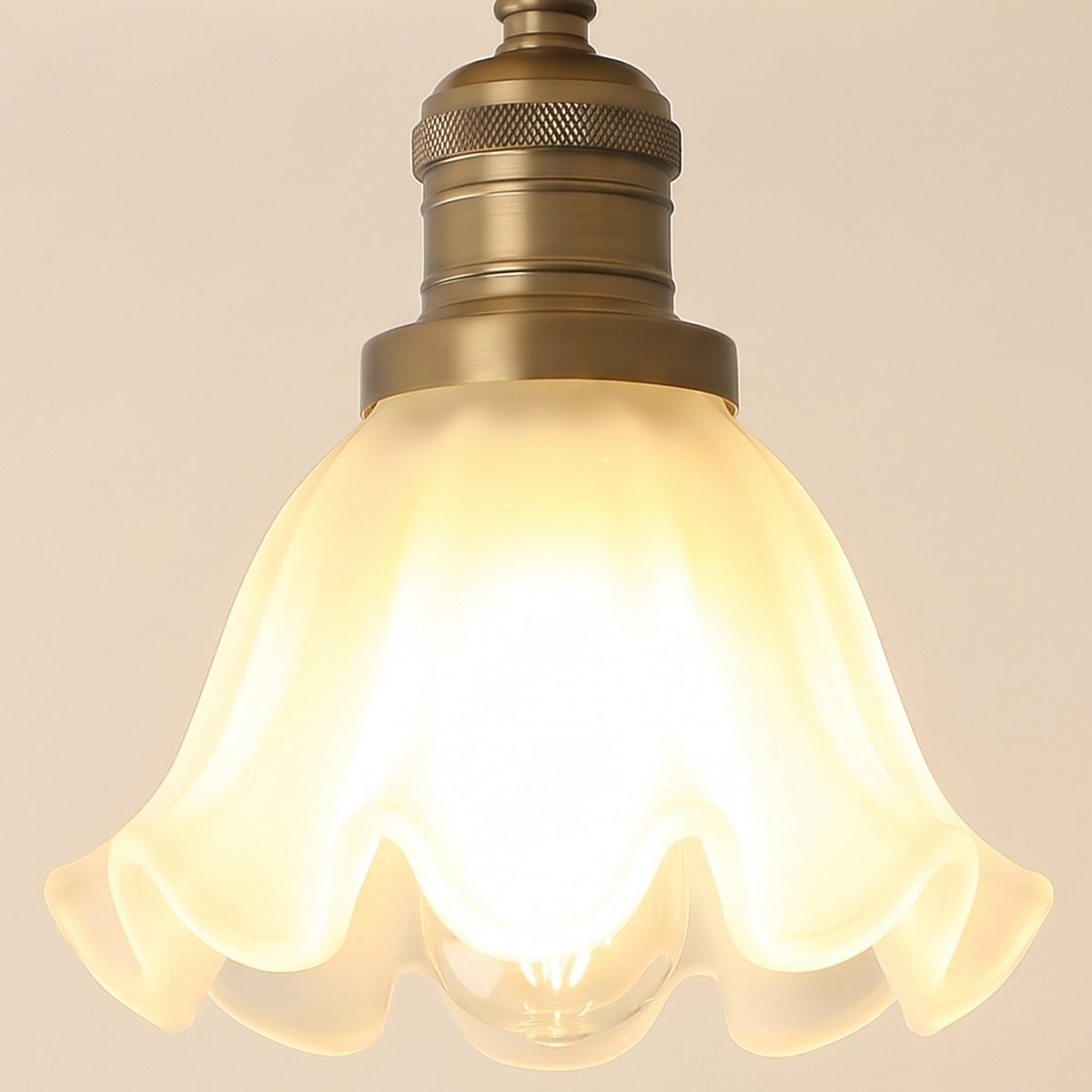 Close up of the Hoxne frosted glass tulip with its ruffled rim and the antique brass lamp holder, lit