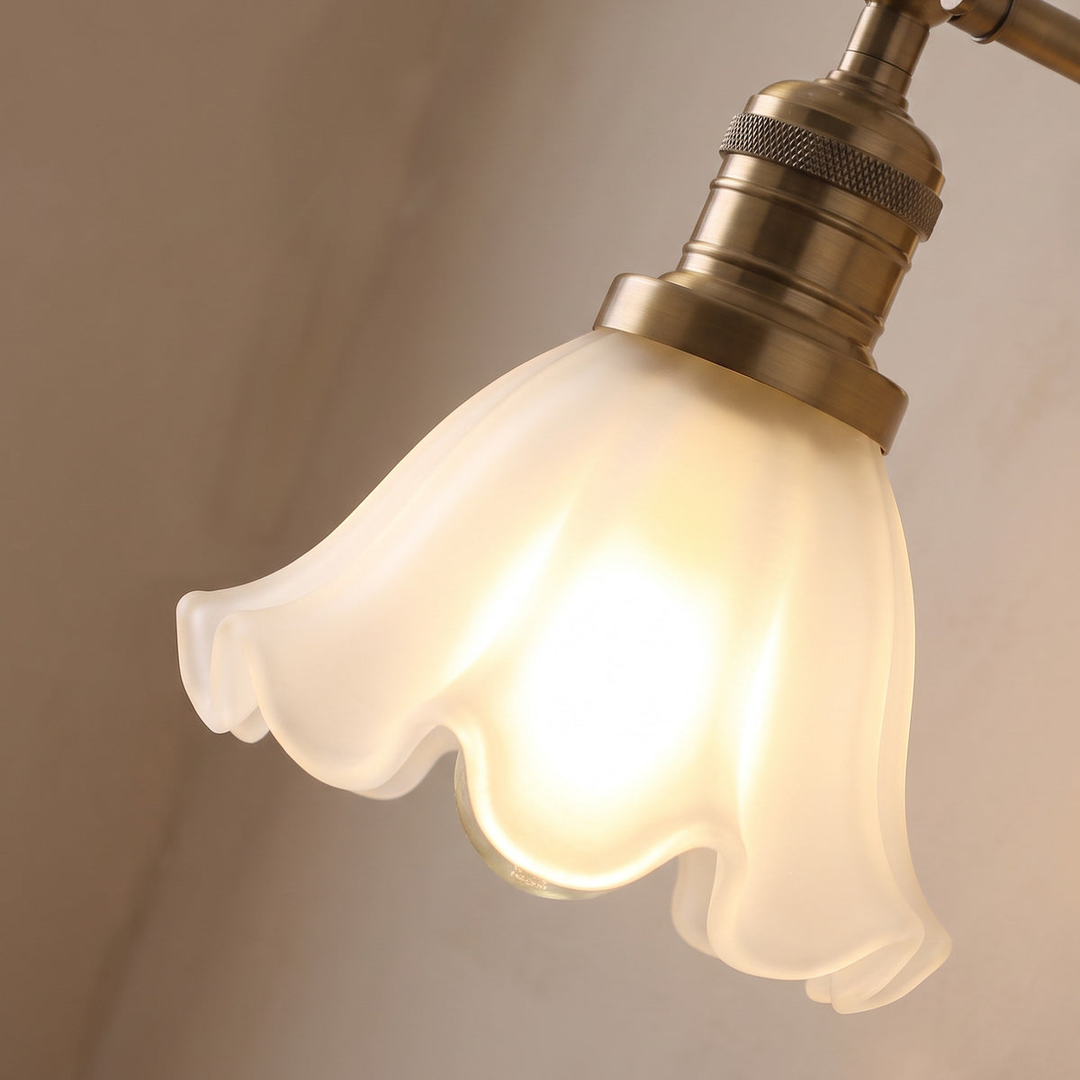 Close up of a lit Hoxne shade showing the ruffled frosted glass rim and the knurled antique brass lamp holder