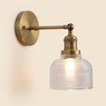 Ixworth wall light in antique brass with a clear prismatic glass bell shade, lit, cream background