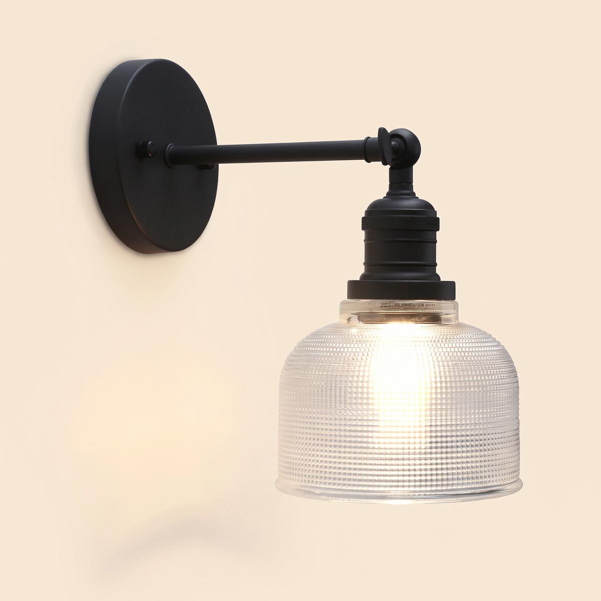 Ixworth wall light in black with a clear prismatic glass bell shade, lit, cream background