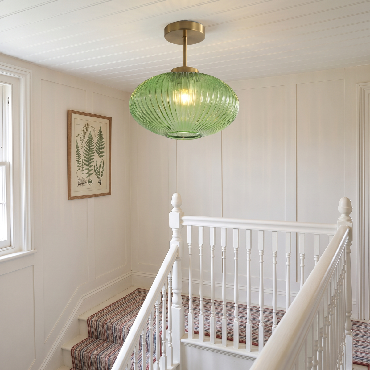 Green Kelsale ribbed glass ceiling light lit above a Victorian staircase landing with white banisters