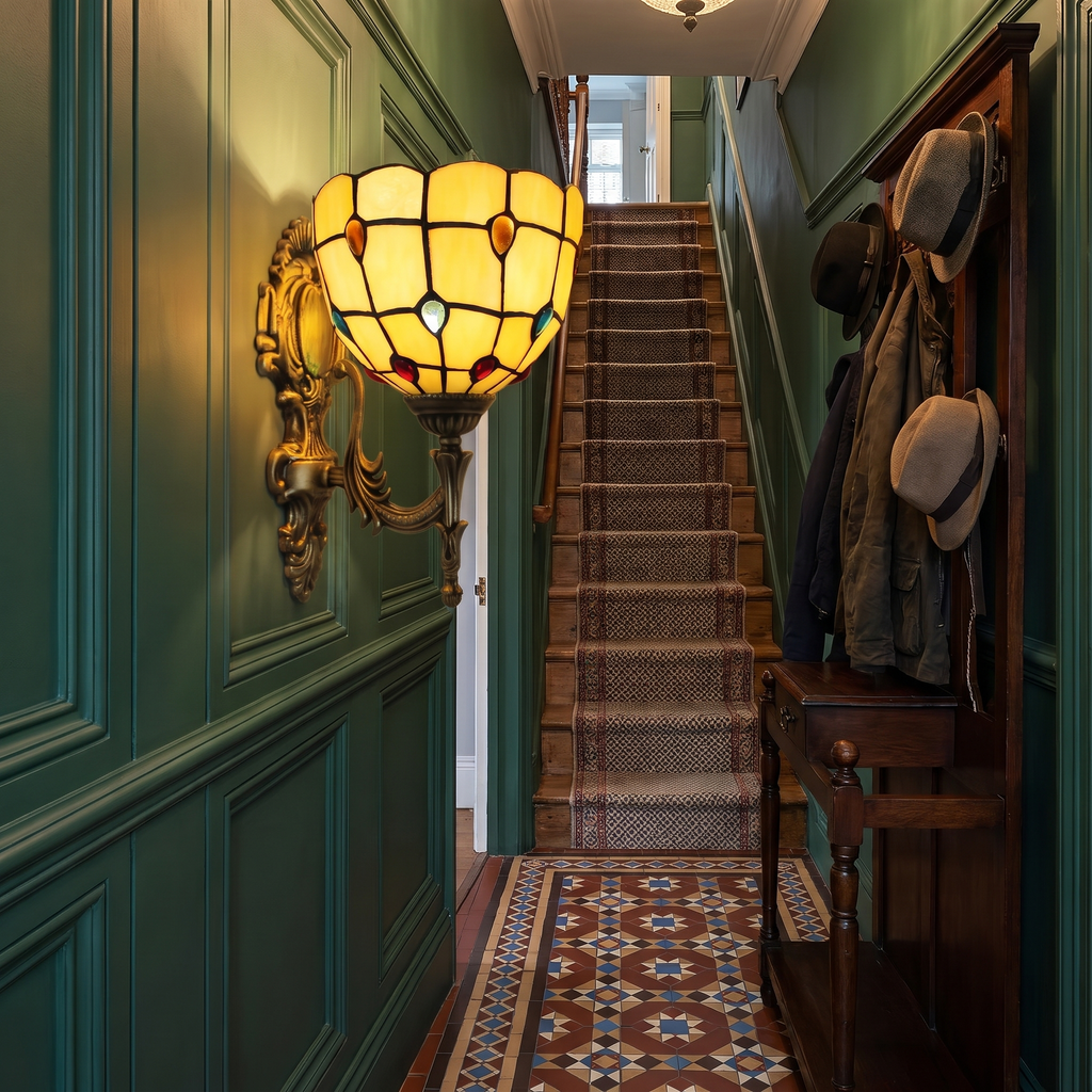 A lit amber Kentwell stained glass wall light on a deep green panelled wall in a Victorian hallway with encaustic floor tiles