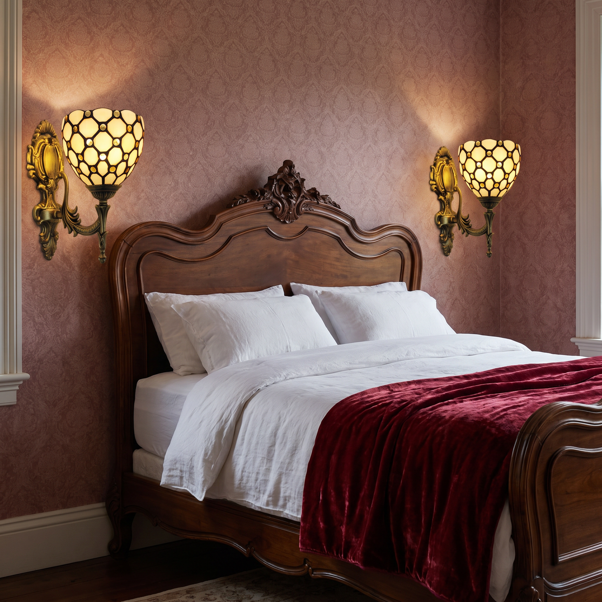 A pair of lit ivory Kentwell wall lights either side of a carved wooden bed in a Victorian style bedroom