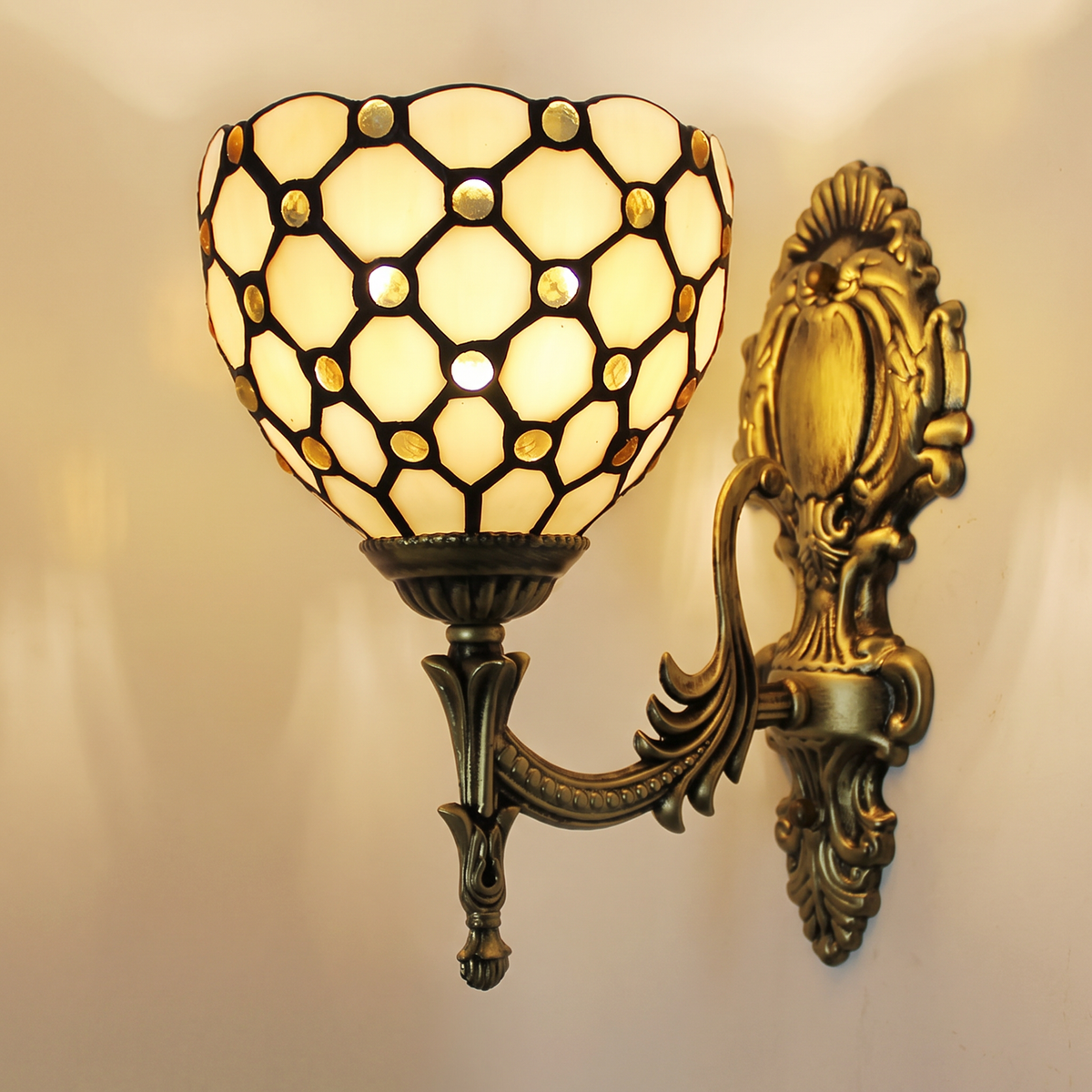 Kentwell wall light, an ivory leaded glass lattice shade with amber glass jewels on an ornate antique bronze arm, lit, cream wall