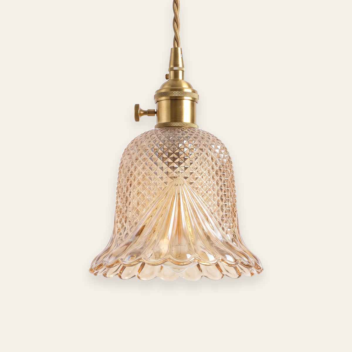 Lavenham cut glass bell pendant light in amber glass with a brass lamp holder on a cream background