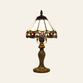 Melford stained glass table lamp, an ivory leaded glass shade with a scalloped border of red glass jewels on a dark bronze finish base, lit, cream background