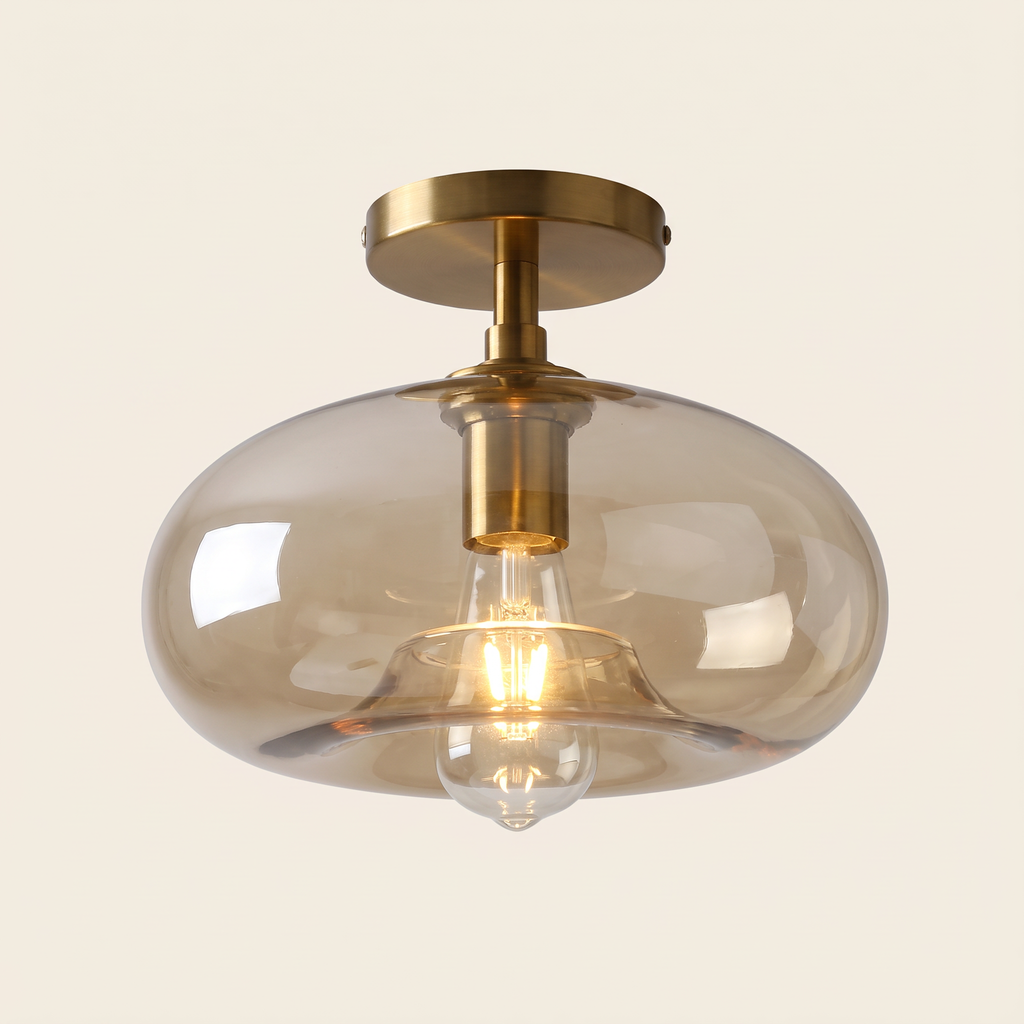 Mendham semi flush ceiling light with a wide pebble shaped amber glass shade on a brushed brass stem and ceiling plate, cream background