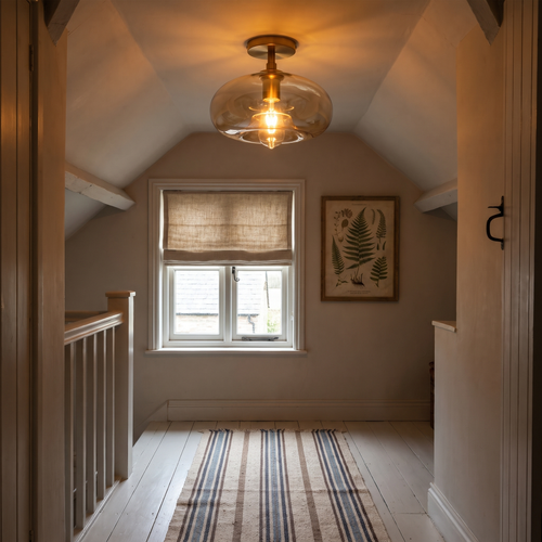 A lit Mendham amber glass ceiling light on the sloping ceiling of a cottage loft landing
