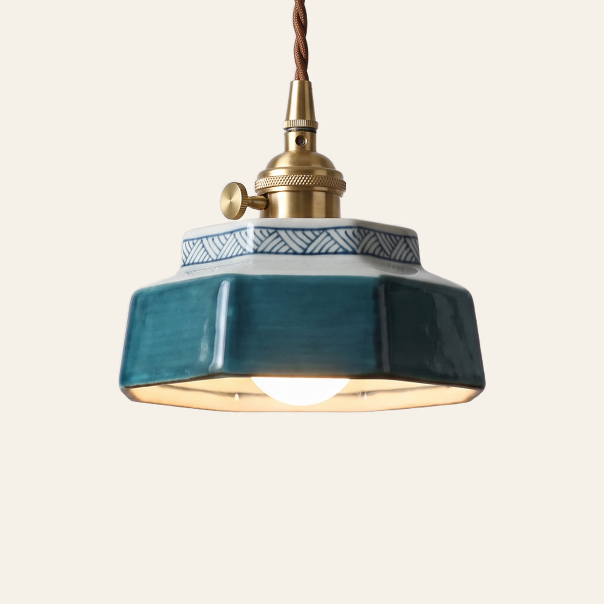 Mettingham pendant light, a small six sided deep teal ceramic shade with a painted key pattern collar on a brass finish holder with a turn switch, lit, cream background