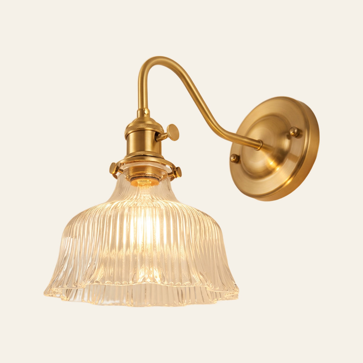 Nayland wall light with a fluted clear ribbed glass bell shade on a brass swan neck arm, lit