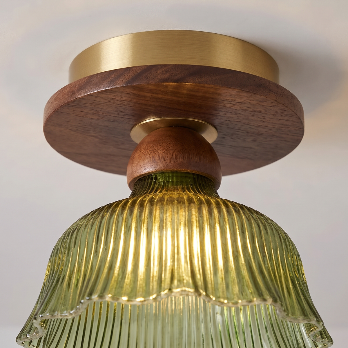 Close up of the Nayland semi flush: brass ceiling plate, walnut tone wood disc and neck, and the ribbed green glass glowing