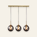 Orla three light smoked glass pendant on a brass bar, cream background