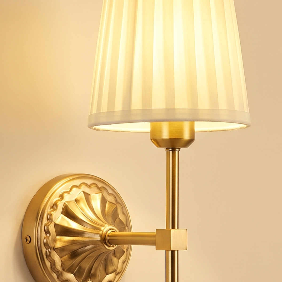 Close up of the embossed rosette backplate, gold finish stem and cream pleated shade of the Palgrave wall light