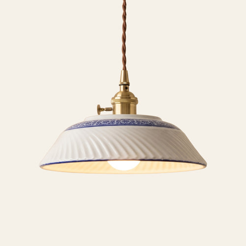 Reydon pendant light, 25.5 cm, a shallow white porcelain shade with swirled ribs and a cobalt blue and white band, on a brass finish holder with a turn switch, lit, cream background