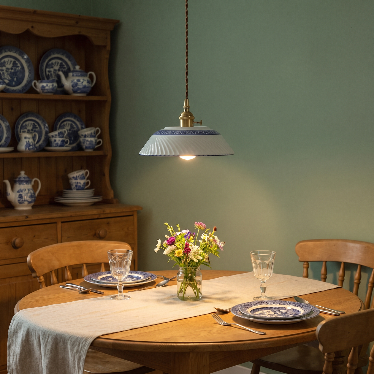 A lit Reydon pendant light over a round oak dining table laid with blue and white plates