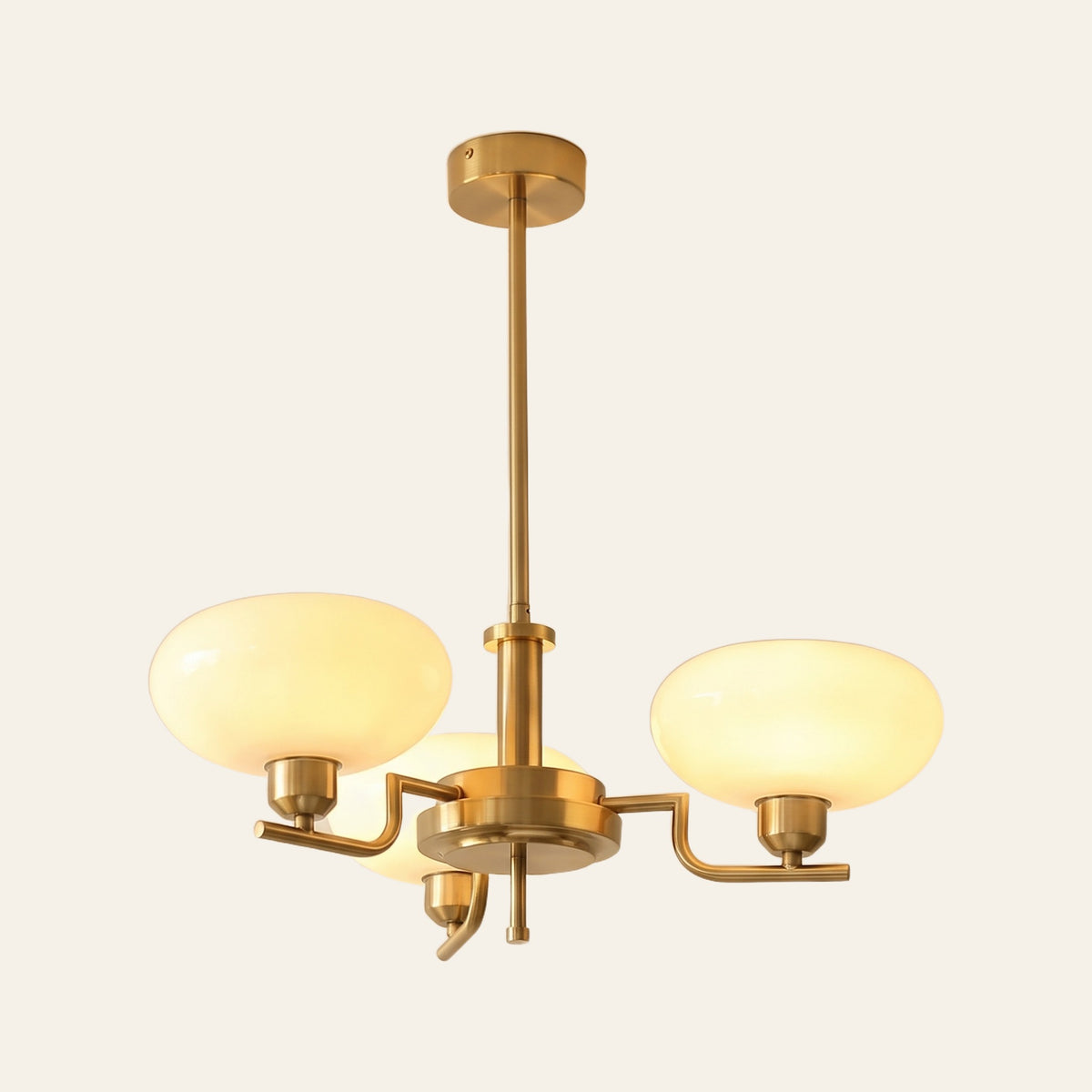 Saxmundham chandelier with three curved gold finish arms and upturned cream opal glass shades, lit, cream background