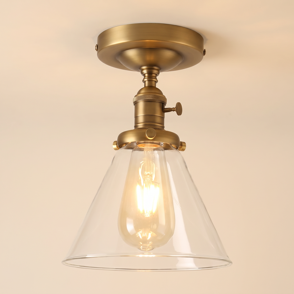 Shotley semi flush ceiling light in antique brass with a clear glass cone shade, lit, cream background