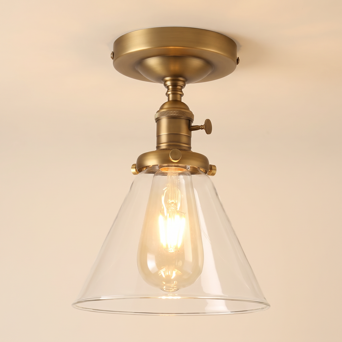 Shotley semi flush ceiling light in antique brass with a clear glass cone shade, lit, cream background