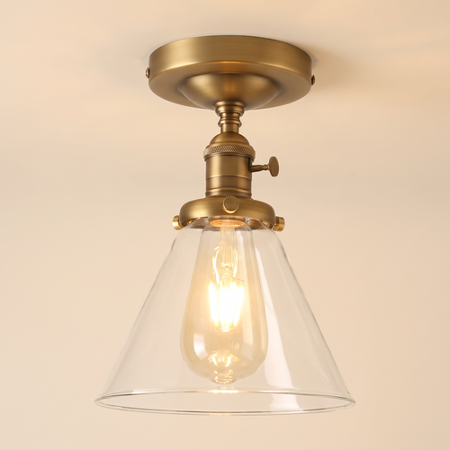Shotley semi flush ceiling light in antique brass with a clear glass cone shade, lit, cream background