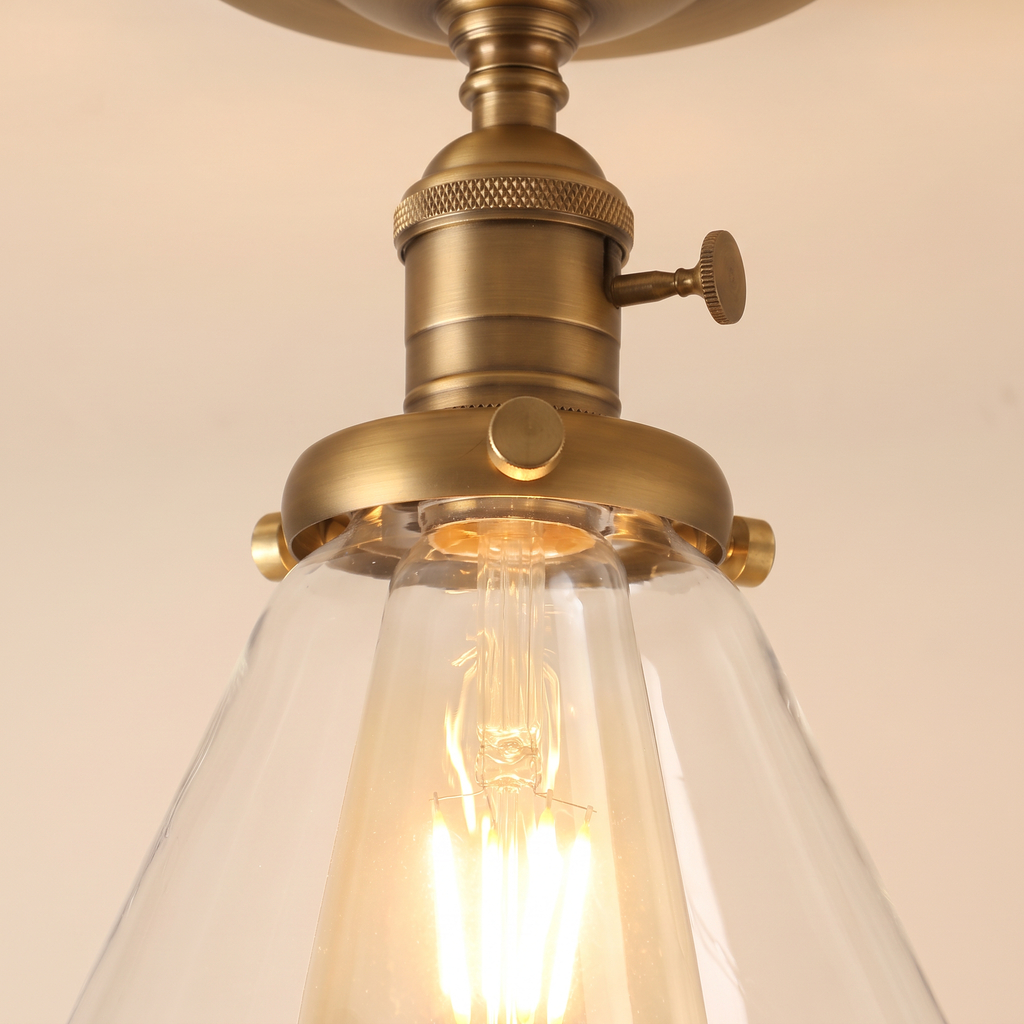 Close up of the Shotley clear glass cone and the knurled antique brass holder with its turn knob, lit