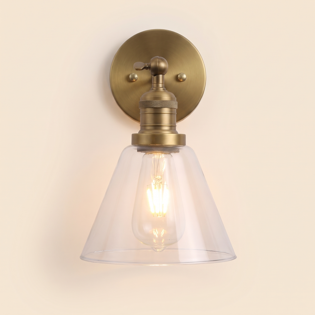 Shotley wall light in antique brass with a clear glass cone shade, lit, cream background