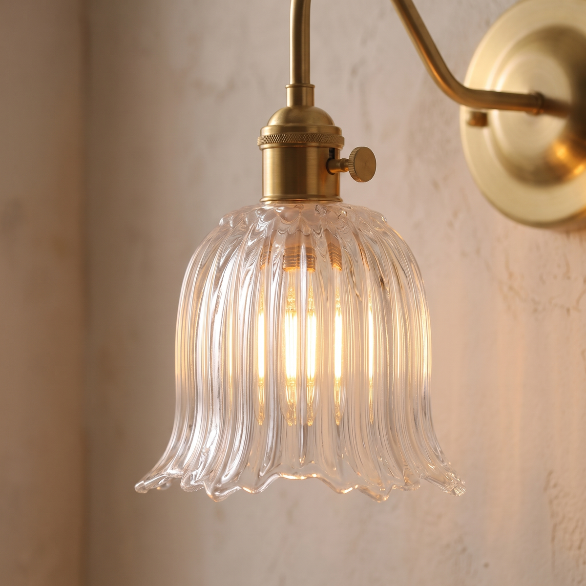 Close up of the clear Sibton fluted glass bell with its scalloped hem and brass turn knob holder, lit