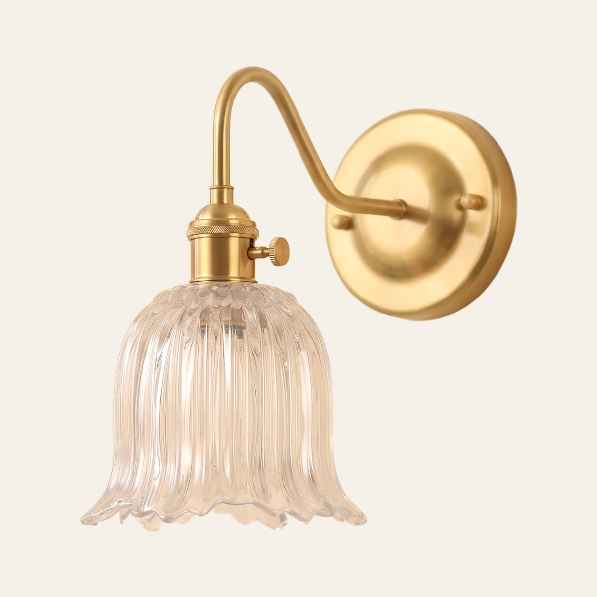 Sibton wall light with a clear fluted tulip glass bell on a brass swan neck arm, cream background