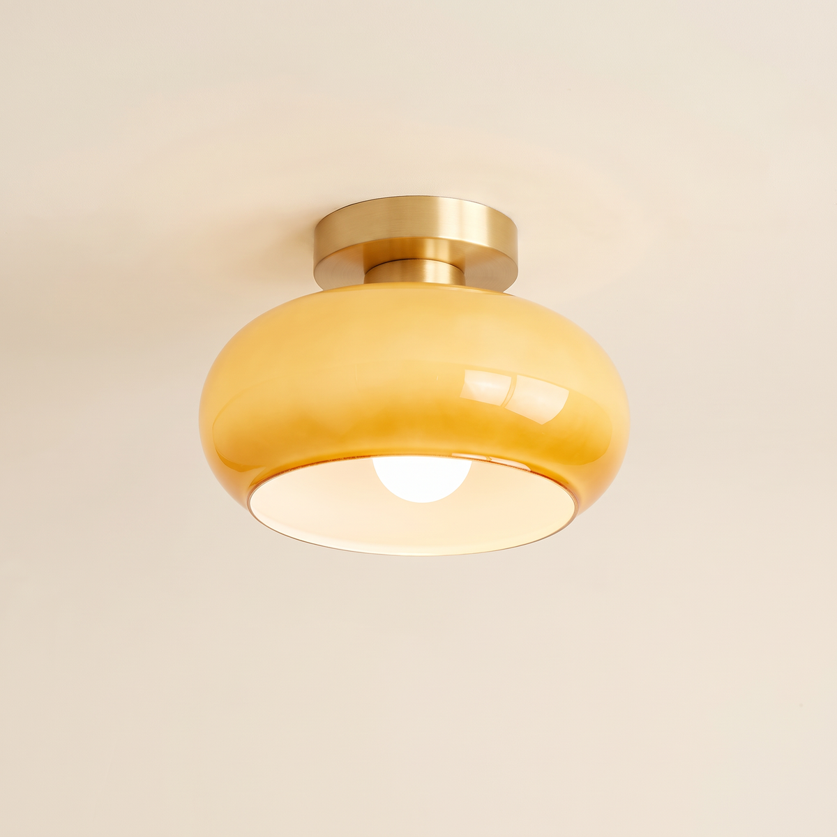 Stradbroke semi flush ceiling light with a rounded caramel glass mushroom shade on a brass finish ceiling plate, cream background