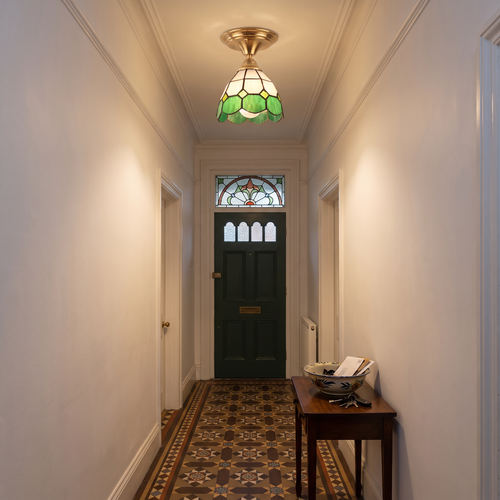 A lit Theberton green stained glass ceiling light in a cottage hallway