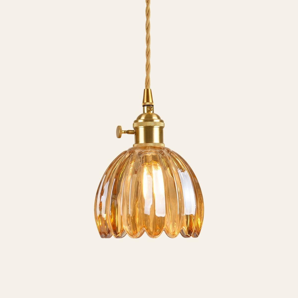 Ufford ribbed glass bud pendant light in honey amber glass on a brass holder with a twisted cord, cream background