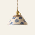 Wilby pendant light, a handmade ceramic coolie shade with blue daisies on a speckled cream glaze and a brass finish holder with a turn switch, lit, cream background