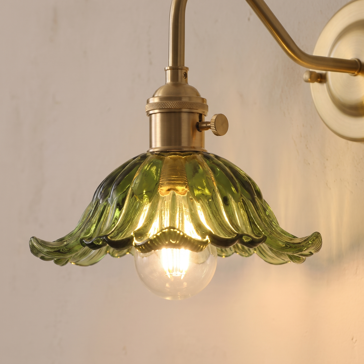 Close up of the green Wissett petal glass shade, globe bulb and brass turn knob holder, lit