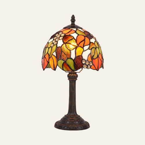 Woolpit stained glass table lamp in the Autumn Leaf design, orange, amber and green leaves with pale glass jewels, lit, on a bronze tone base, cream background