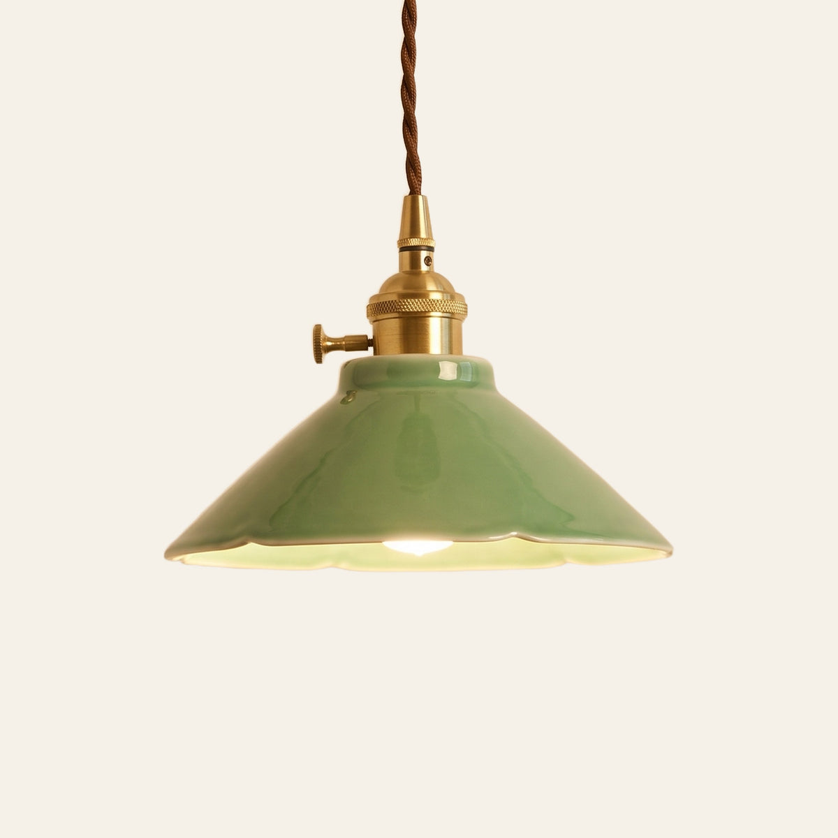 Wortham pendant light, a glossy jade green glazed ceramic coolie shade on a brass finish holder with a turn switch, lit, cream background
