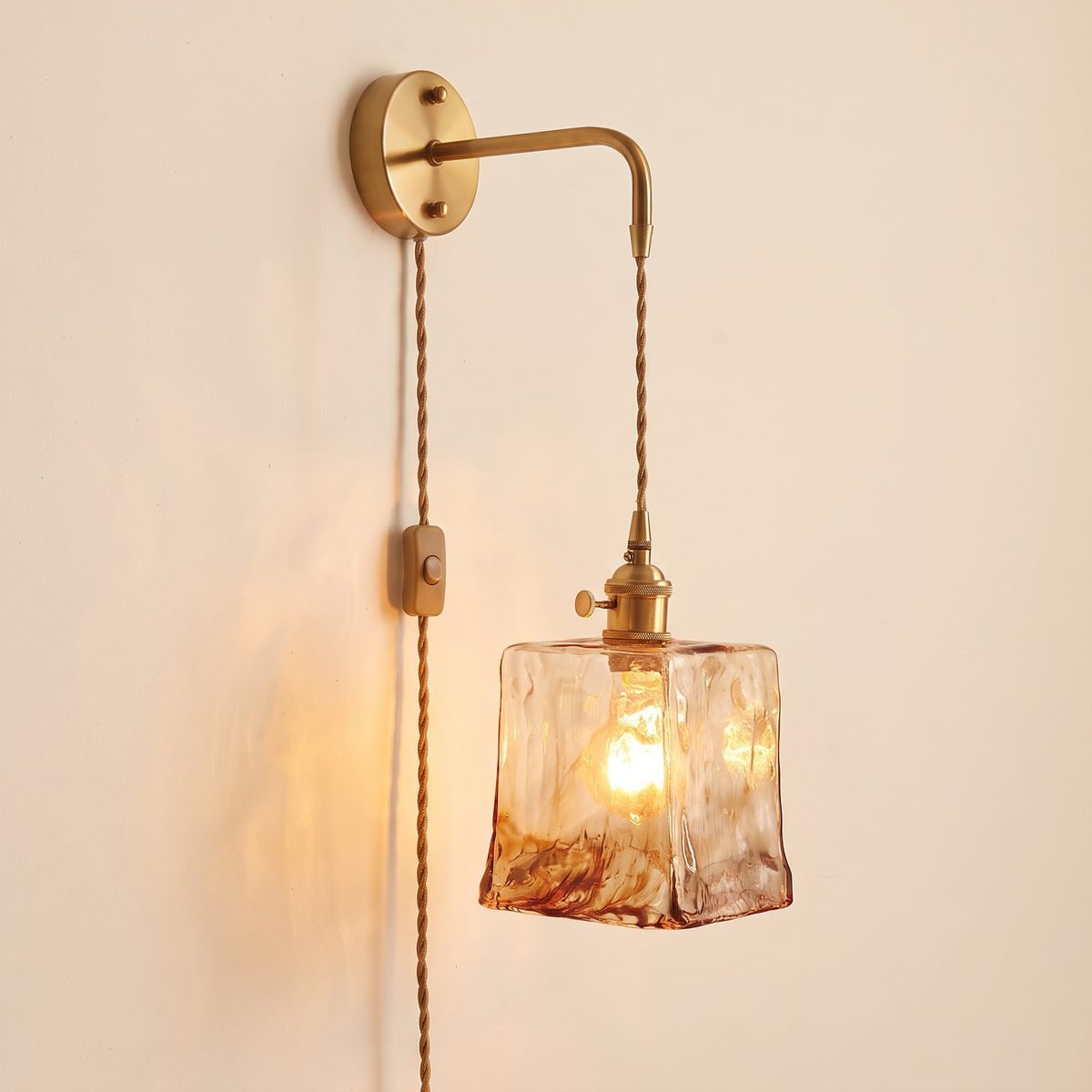 Yaxley plug in wall light with a square amber hammered glass shade on a braided cord, lit, cream background