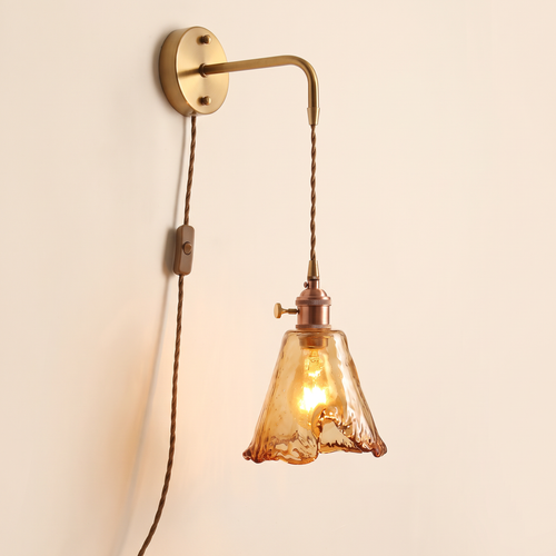 Yaxley plug in wall light with a small amber hammered glass tulip shade on a braided cord, lit, cream background